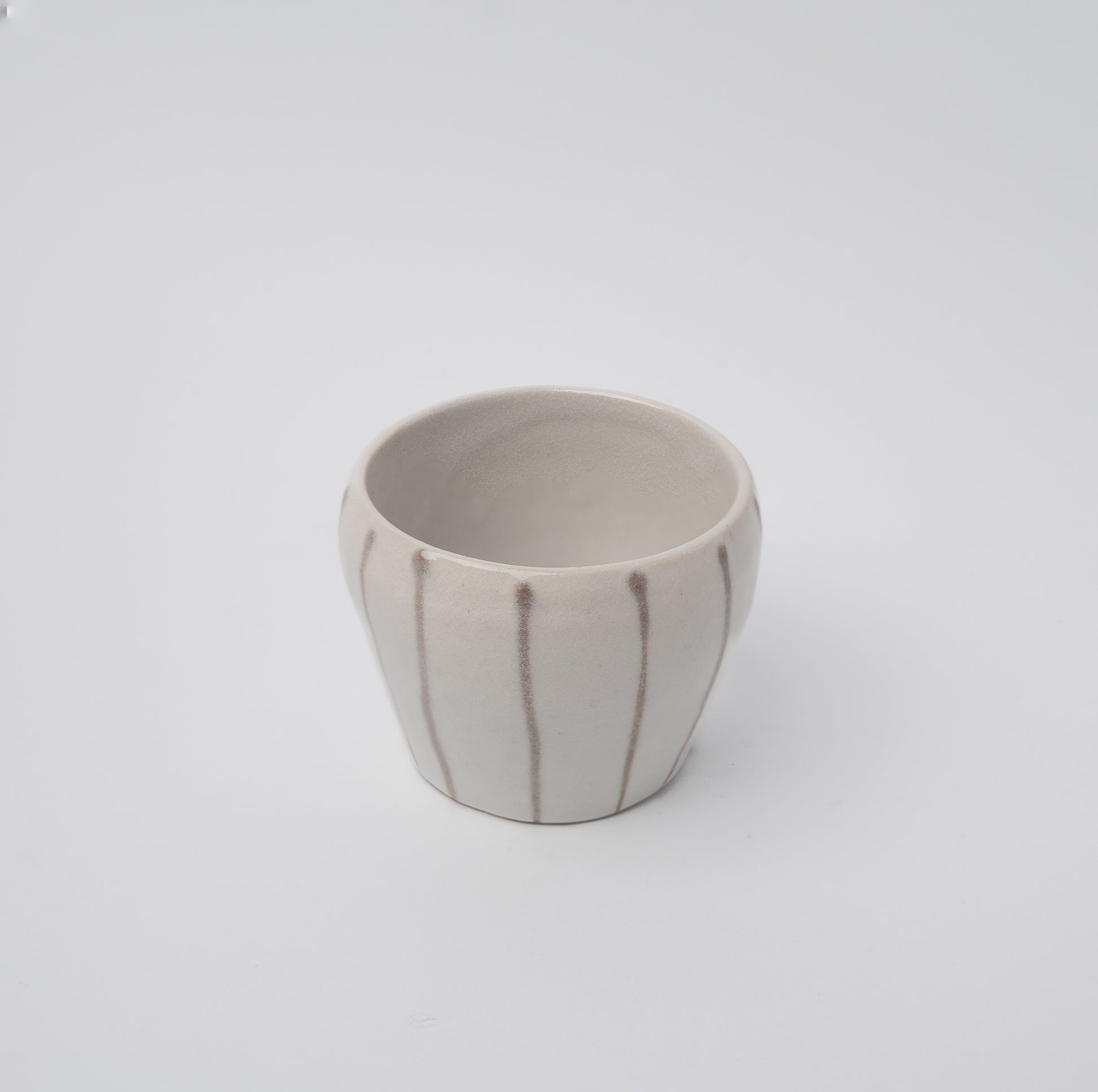 White ceramic tea cup with vertical brown stripes, minimalist Japanese design.
