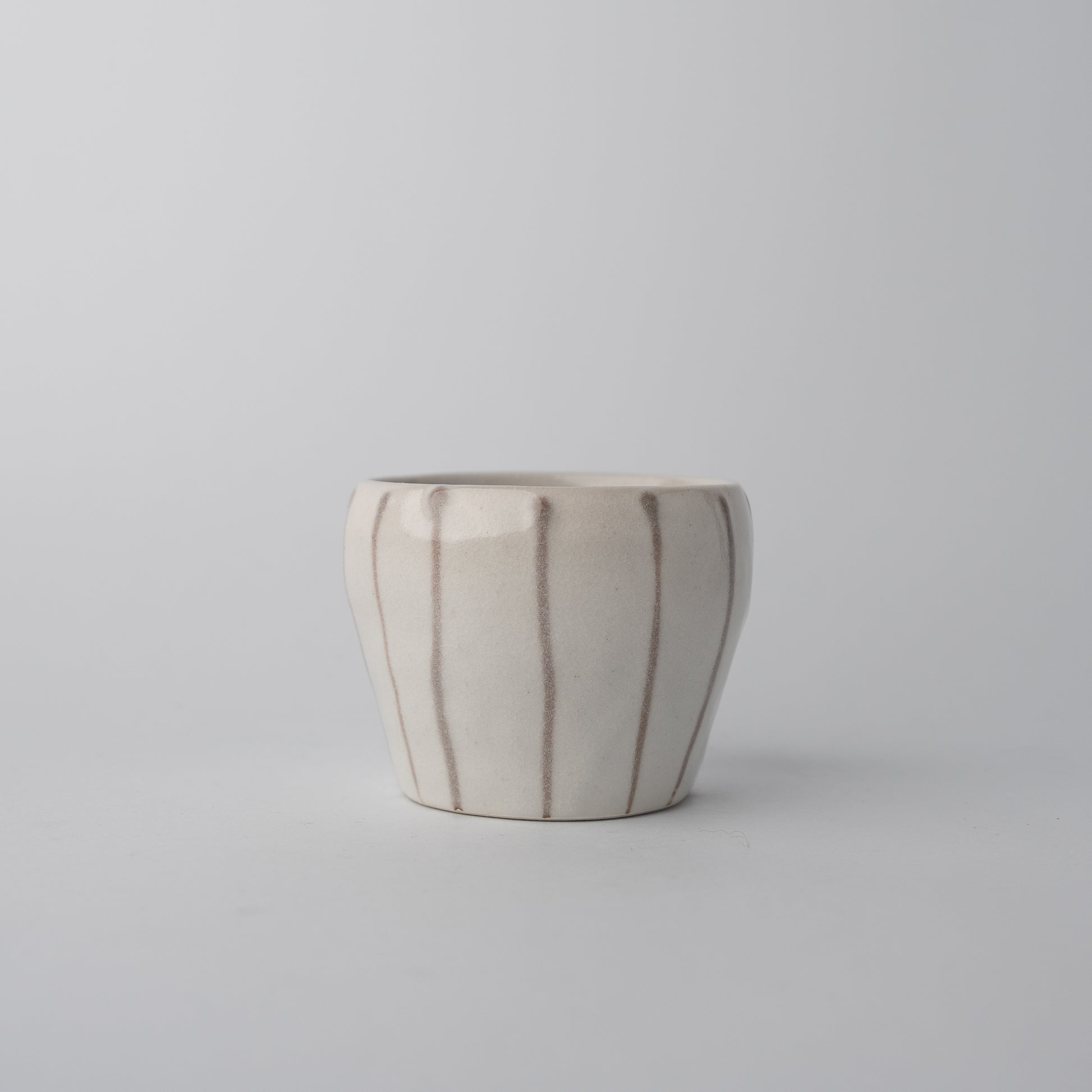 White ceramic tea cup with vertical brown stripes, minimalist Japanese design.
